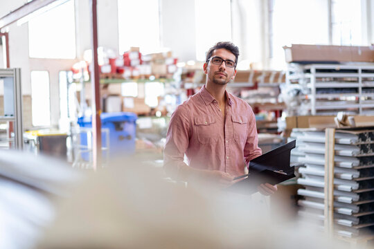 Businessman holding file folder and examining inventory in factory