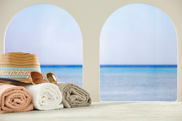 Towels, hat and sunglasses on white furniture with tropical beach and sea background. Summer table background for montage product display.