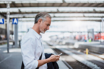 Businessman using smart phone and standing at railway station