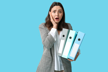 Shocked young businesswoman with folders on blue background