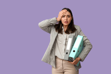 Shocked young businesswoman with folders on lilac background