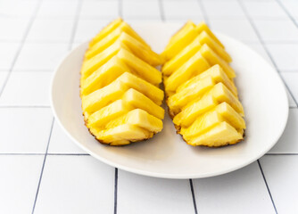 Two beautifully sliced pineapple halves on a white plate, placed on a tiled surface