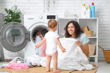Young mother with her cute little baby doing laundry in bathroom