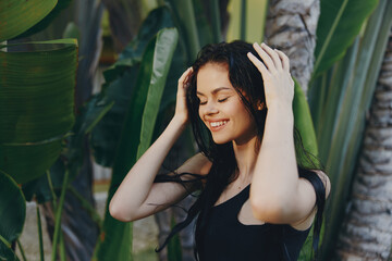 Woman in black top standing with hands on head in front of palm trees on sunny day