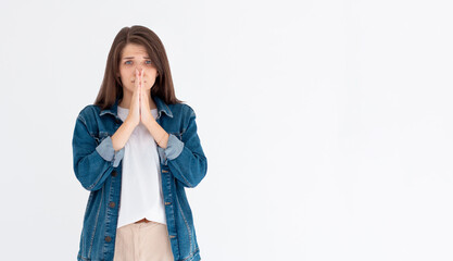 Portrait of imploring girl tilts head, purses lips, looks sadly at camera, makes praying gesture,...