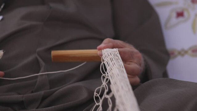 Senior man is knitting traditional fishing net, hands in frame