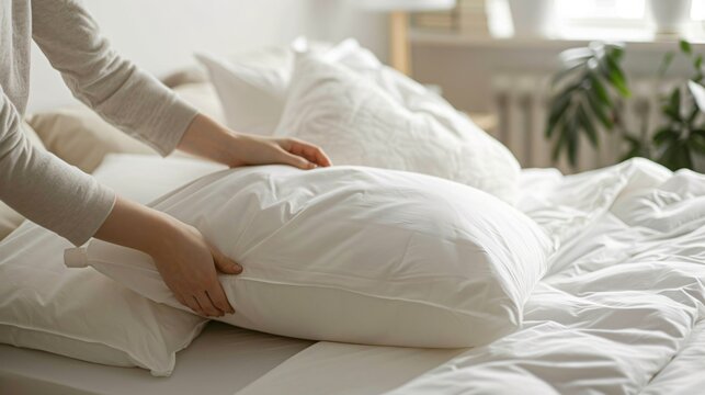 Hands pulling up a sheet and arranging pillows on a neatly made bed in a minimalist bedroom
