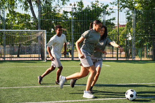 Three young adult soccer players are running on a field on a sunny day
