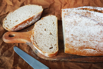Homemade grain bread on a wooden board next to a knife on a linen napkin