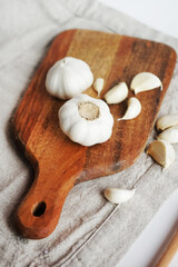 Whole garlic and cloves on a wooden board next to a knife on a linen napkin