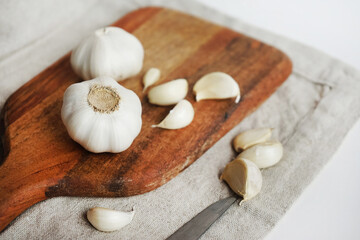 Whole garlic and cloves on a wooden board next to a knife on a linen napkin