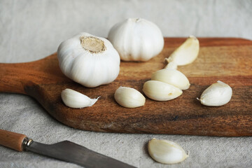 Whole garlic and cloves on a wooden board next to a knife on a linen napkin