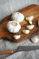 Whole garlic and cloves on a wooden board next to a knife on a linen napkin