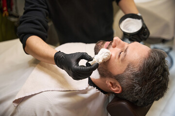 Stylist using professional shaving brush to apply white shaving foam