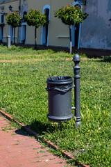 Obraz premium Public rubbish bin in a park - Serbia. Empty trash can in the park. Black bin in park. Black metal garbage bin in park.