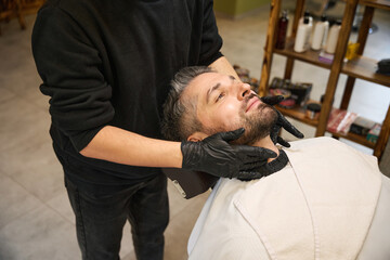Barber applying special balm or oil into male client beard