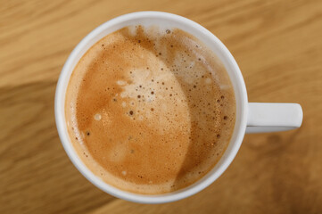 Poranna kawa ze spienionym mlekiem, kubek widok z góry oświetlany promieniami słońca 