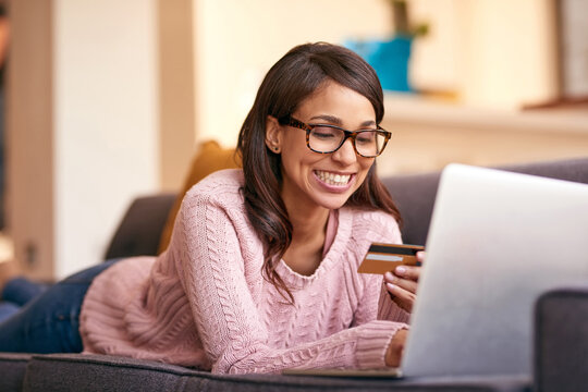 Debit card, laptop and woman relax in home with happiness for paying bills with debt free lifestyle. Smile, computer and person on sofa with internet banking app to apply for mortgage in apartment.