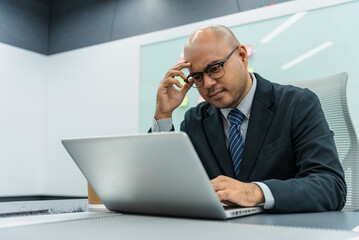 Tired young asian man businessman worker lawyer at work. He has a headache keeps his hands on his head sits at a desk in the office. Unity of position executive, manager and employee concept.