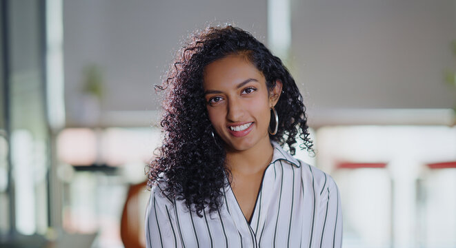 Indian close up of curly hair young adult gen z boss woman owner lady face standing proud look cam indoor day office happy expert teen girl female agent staff do pose head shot video job work place
