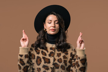 Stylish woman praying with crossed fingers on beige background.Lady begs someone