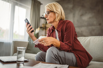 Mature woman hold the medicine and read instructions on mobile phone