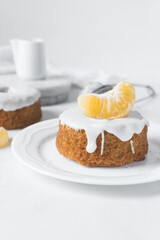 Iced mini bundt cake on a white tray, vanilla bundlette cakes with a clementine segment on a white background, small vanilla bundt cakes with an icing glaze