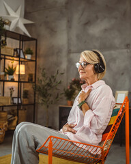 Mature woman sit on chair with headphones and have guided meditation
