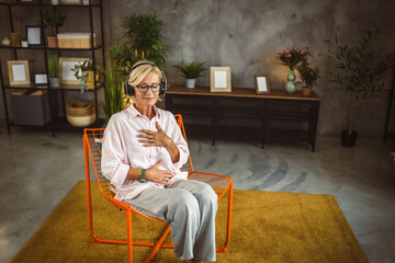 Mature woman sit on chair with headphones and have guided meditation