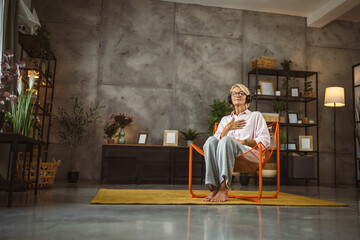 Mature woman sit on chair with headphones and have guided meditation