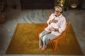 Mature woman sit on chair with headphones and have guided meditation