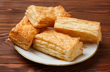 Delicious puff pastries in a white plate on a wooden table. Selective focus