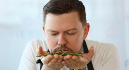 Portrait of professional chef smell twig of rosemary, herb add to dish, better taste with greenery. Cooking as hobby, enjoy delicious food. Eating concept