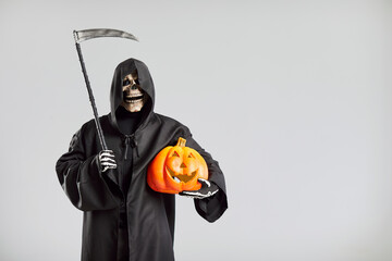 Man in grim reaper death costume with black cloak and hood standing isolated on studio gray...