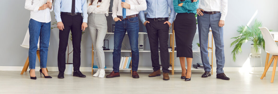 Legs of unrecognizable business people men and women standing in a row in office. Cropped shot of a group of employees in formal clothes standing on a meeting. Teamwork concept. Banner.