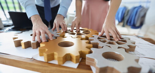 Close-up of businesspeople put wooden gears on workplace together, work in team. Teamwork,...