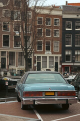 A classic blue car parked along a picturesque canal in Amsterdam, showcasing the city's historic architecture and charming urban landscape. This image captures the essence of Amsterdam's
