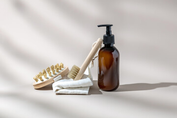 Wooden brush, massage brush, towel and pump bottle on beige background with shadows