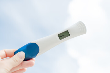 Hand holding a Positive pregnancy test on the sky background. Pregnancy concept. Pregnant electronic test. Digital test