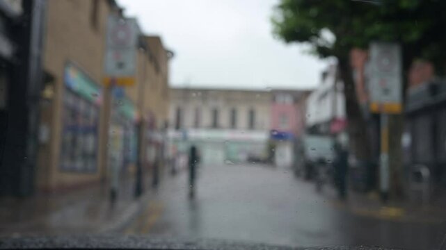 Windscreen wiper clears rain from a car windscreen, seen from inside, background out of focus