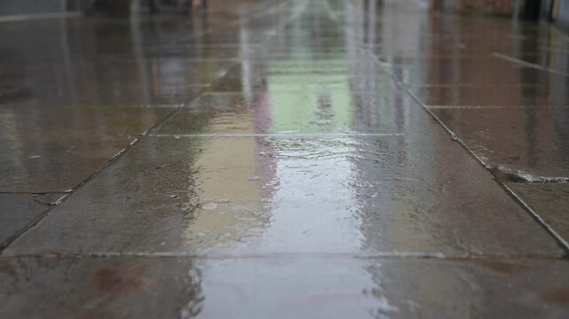 Rain falling on wet pavement, with reflections on the shiny stone