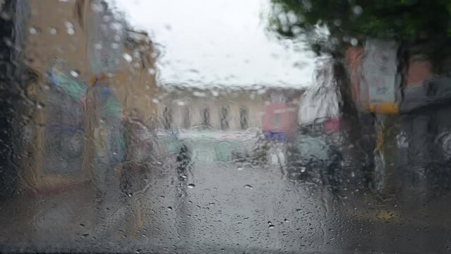 Rain drop run down the glass of a car windscreen, seen from inside, background out of focus