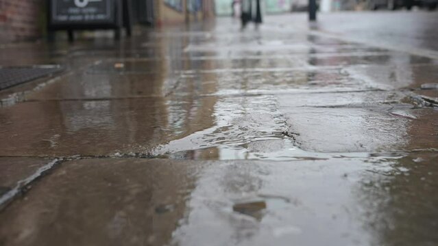 Rain falling on wet pavement, with reflections on the shiny stone