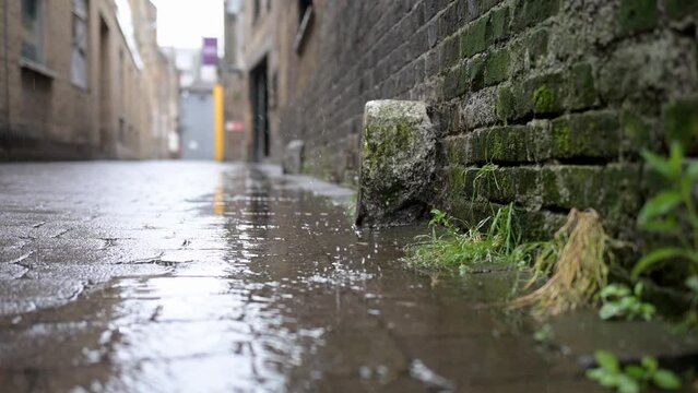 Drips splash to the ground in a wet, rainy alley against an old brick wall