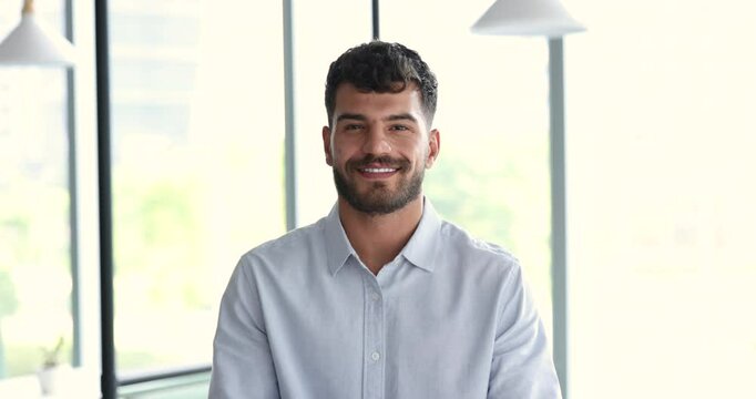 Serious young Arab business man in formal shirt crossing arms at chest, getting happy, cheerful, looking at camera with toothy smile, posing indoors for professional portrait