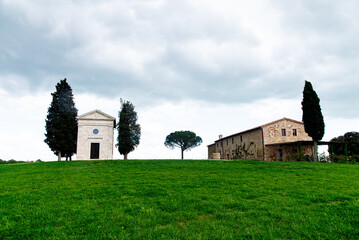 Obraz premium Tuscany, Italy-April 22, 2024: Chapel and Rustic House on Grassy Hill in Tuscany