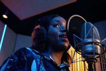 African American young singer singing in microphone and rehearsing her song in studio