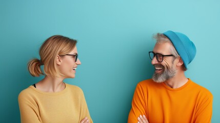 Fototapeta premium Two smiling people wearing glasses, standing against a blue background, engaging in a joyful conversation with crossed arms.