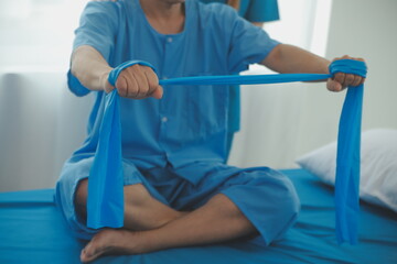 Obraz premium Close up hand patient doing stretching exercise with a flexible exercise band and a physical therapist hand to help in clinic room.