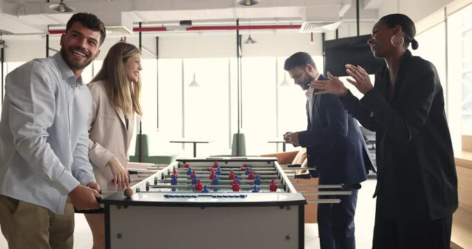 Couple of excited diverse office workers beating team of colleagues in table soccer, giving high five, playing table toy football game, smiling, laughing, enjoying win, success, work break activity